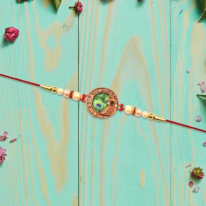 Elegant Rakhi With Peacock Feather Design And Pearl Bead Accents On Red Thread